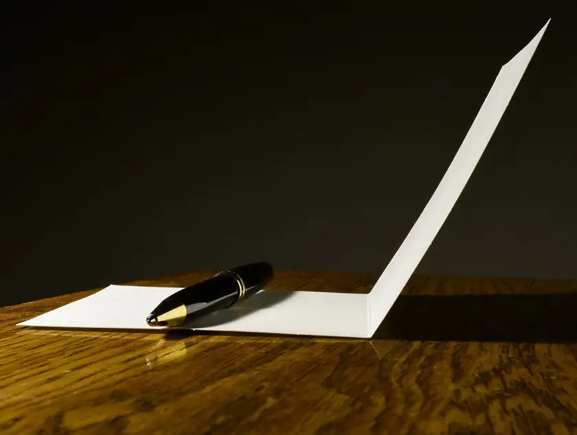 A fountain pen resting on a blank folded card on a wooden table