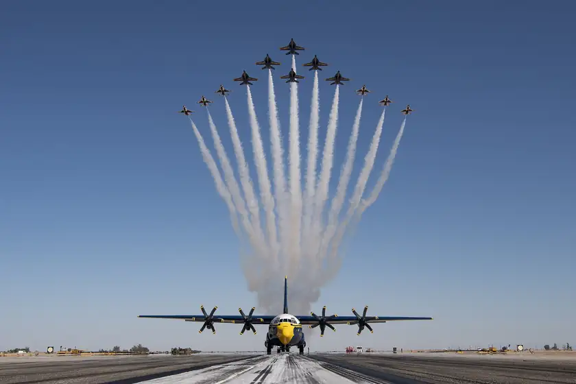 Blue Angels jets flying in formation with smoke trails above a large propeller plane
