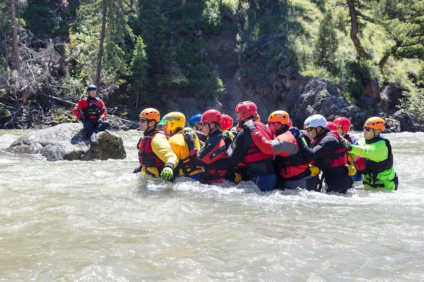 Rescuers in helmets and life jackets move together through a river