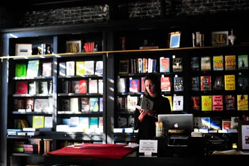 A woman standing in front of tall bookshelves and reading an open book