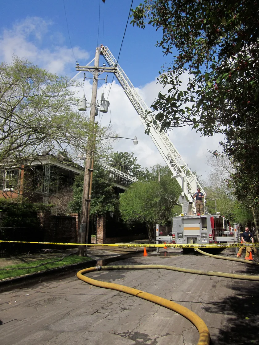 Firefighters on an extended ladder directing a hose at a smoking house