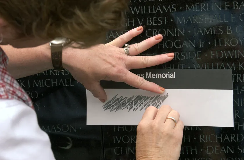 Hands press a sheet of paper against the Vietnam Veterans Memorial to make a pencil rubbing of a name