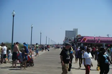 A wooden beach boardwalk lined with shops, with sand on the left and an American flag overhead