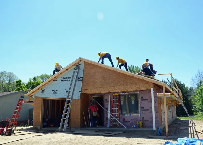 Sailors in uniform framing the wooden walls of a house under construction