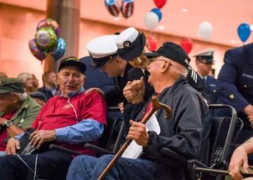 Service members in dress uniforms escorting older veterans through an airport terminal