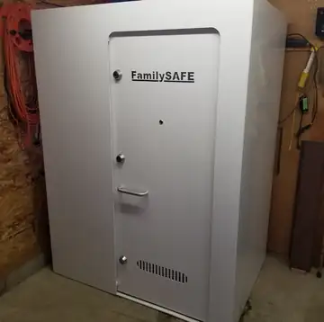A white above-ground storm shelter with a metal door in a garage