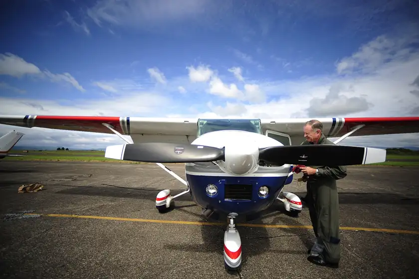 A pilot in a blue uniform checking the oil on a small propeller plane