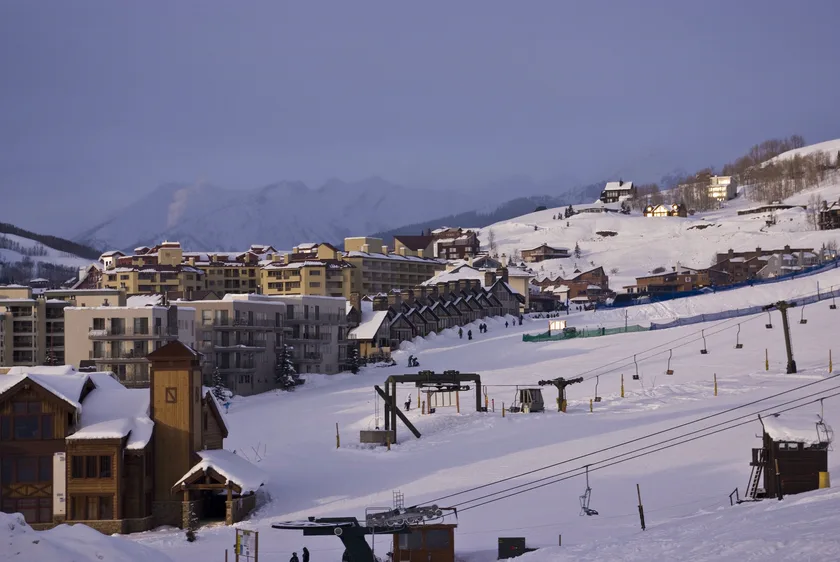Skiers descending a wide snowy slope beneath an overcast sky