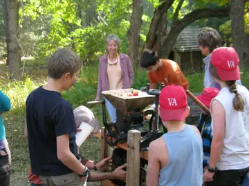 Adults gathered around an apple press in an orchard, with bins of apples nearby