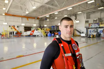 A rescue swimmer in an orange suit being lowered toward the water