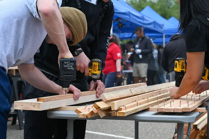 Volunteers assembling wooden bed frames in a large room