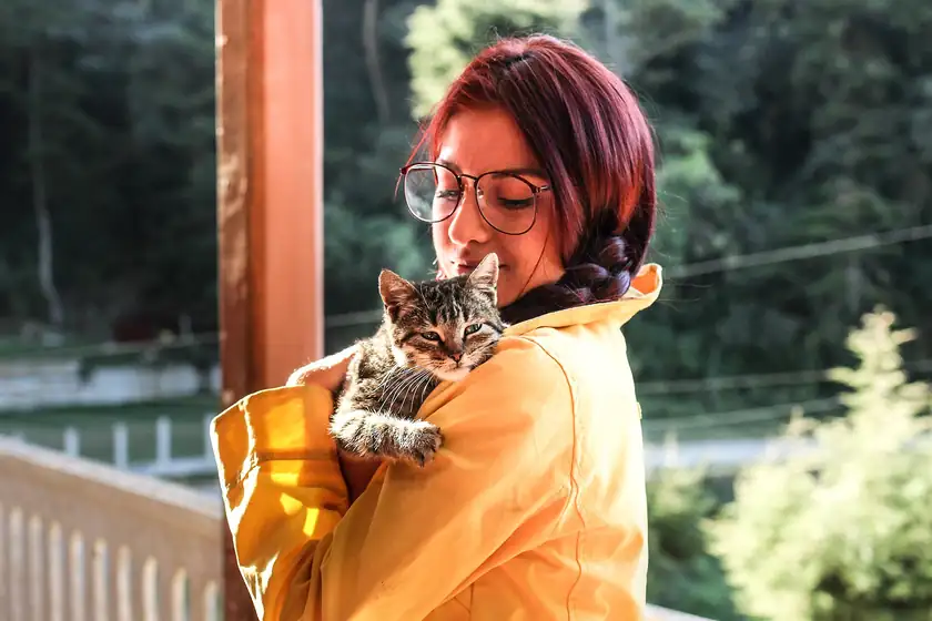 A woman holding a gray cat close against her shoulder