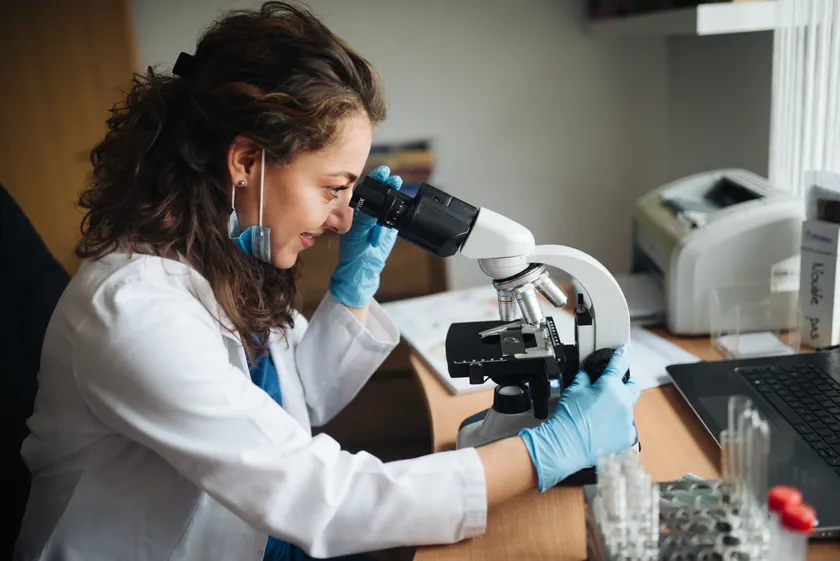 A scientist in a lab coat looking through a microscope