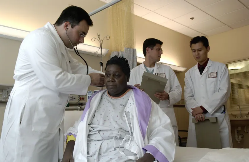 A doctor using a stethoscope to examine an adult patient, with two colleagues nearby