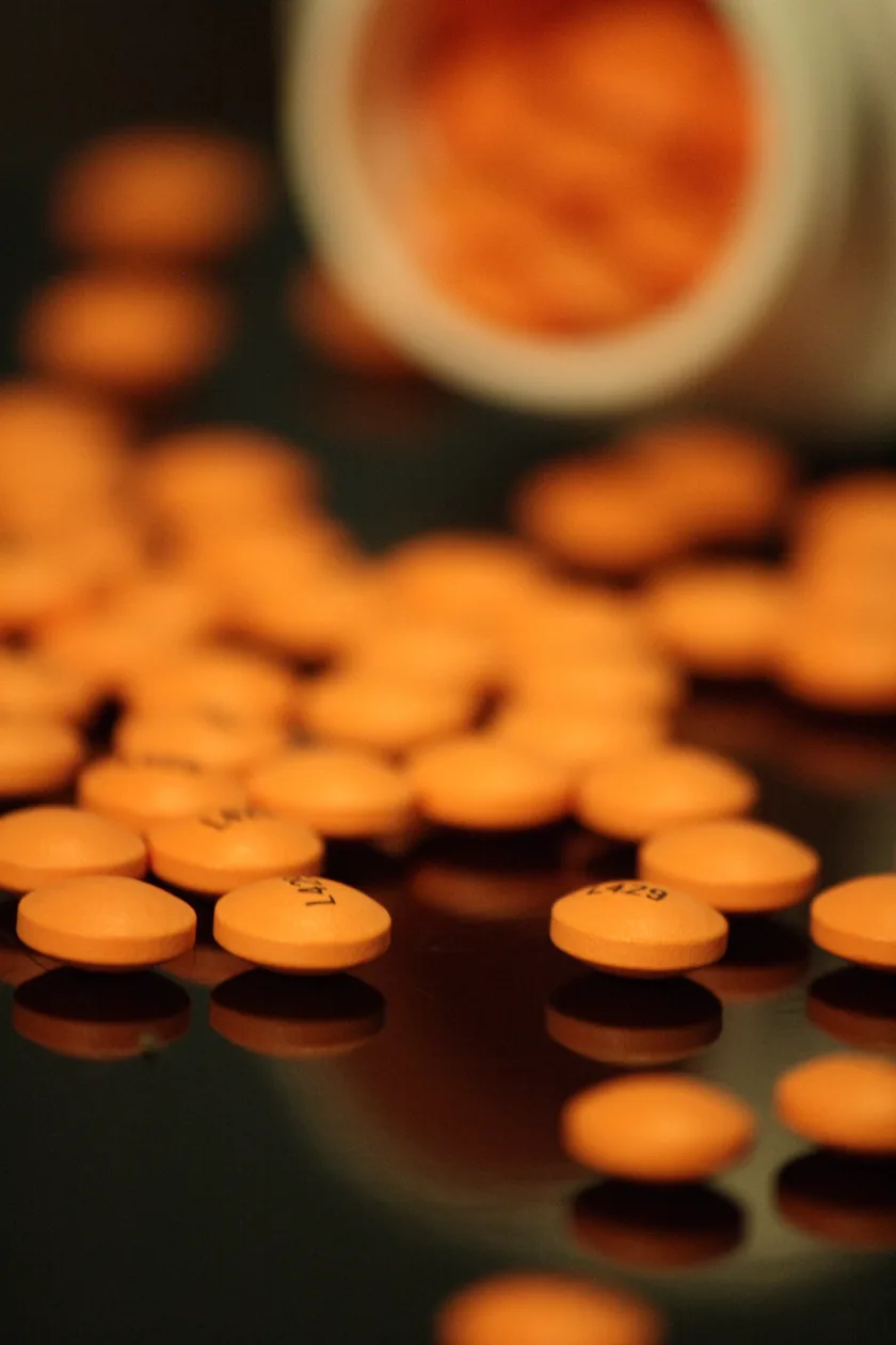A white bottle of regular-strength aspirin with orange tablets spilled beside it