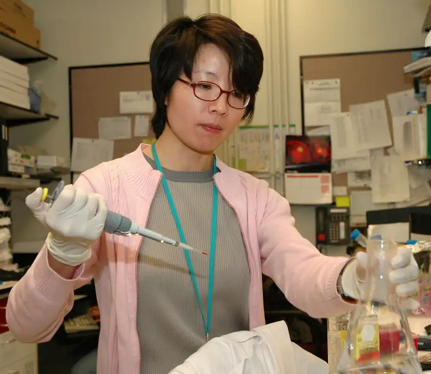 A scientist in a white coat using a pipette at a laboratory bench