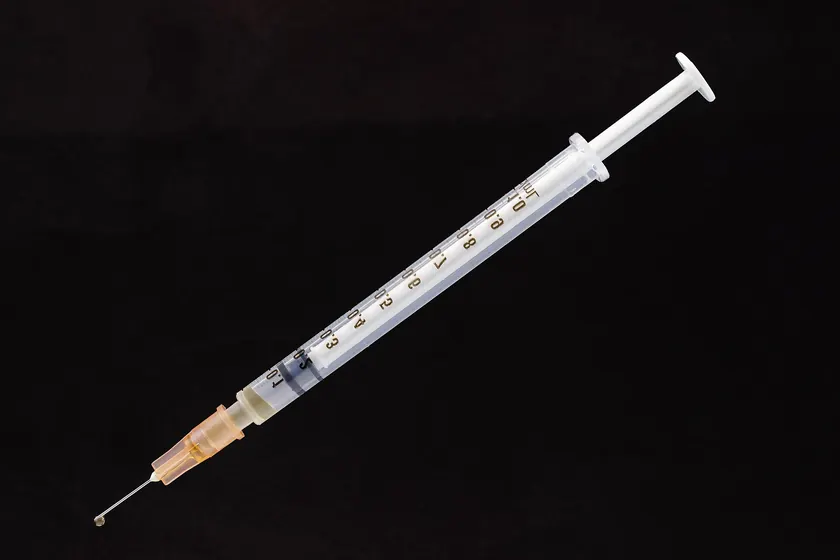 A clear plastic syringe with a capped needle lying on graph paper