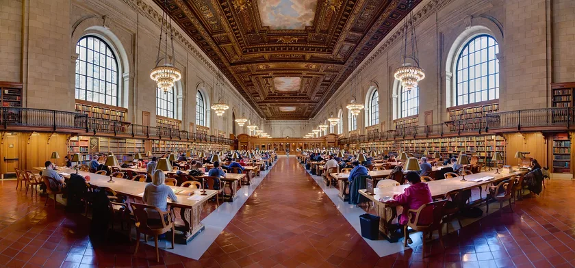 Adults reading and studying at tables in a large public library room