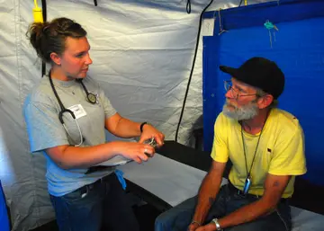 Navy staff members talking with veterans at an outdoor stand-down, with medical tables nearby