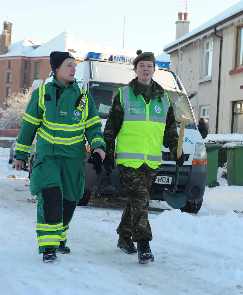 A paramedic and a soldier pushing a patient on a stretcher toward an ambulance
