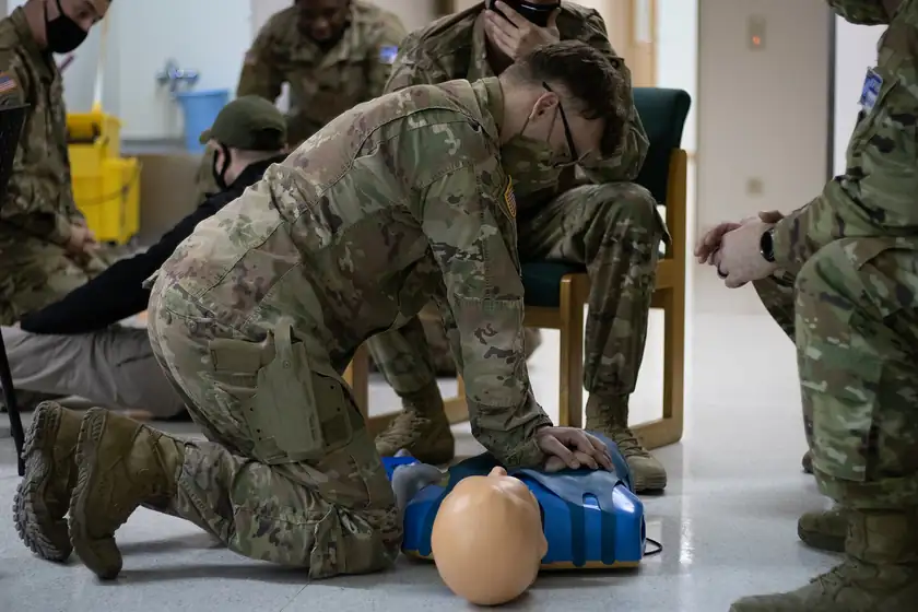 A soldier kneeling and practicing chest compressions on a training manikin