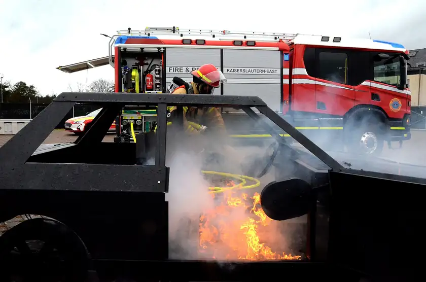 A firefighter in full gear training with a hose beside a fire truck