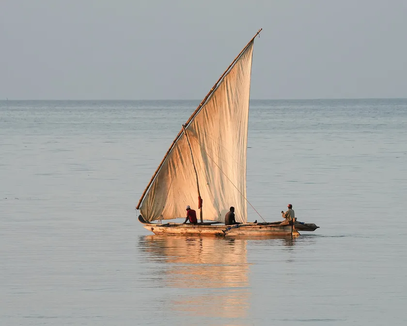 Three people sitting in a wooden sailing boat with a pale lateen sail on calm water
