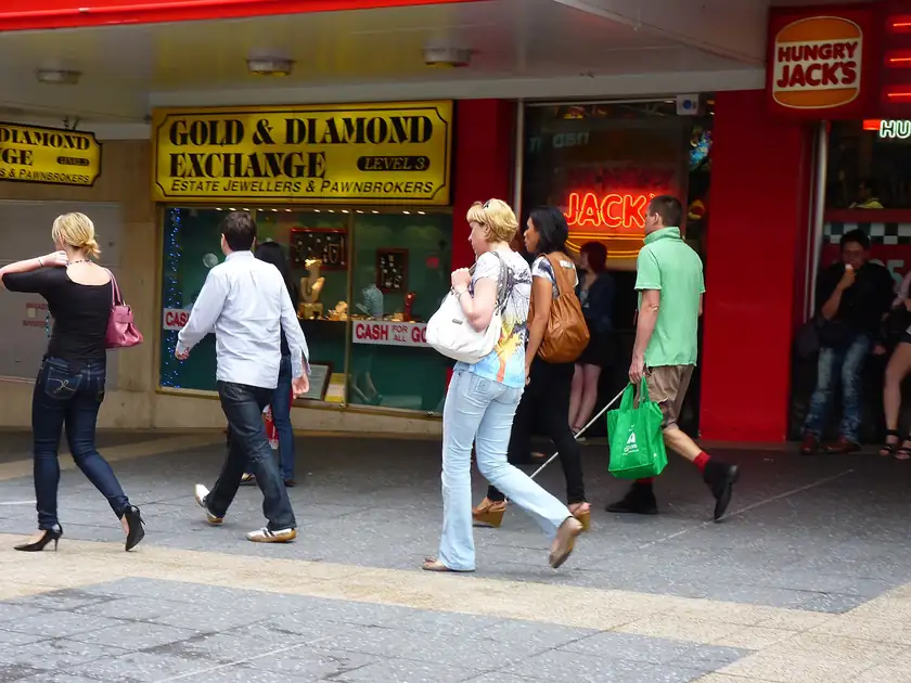 A pedestrian seen from behind using a white cane on a city sidewalk