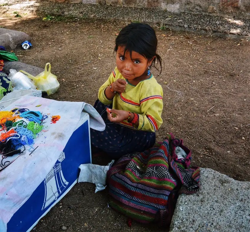 A woman seen from the side working on colorful beadwork at a table