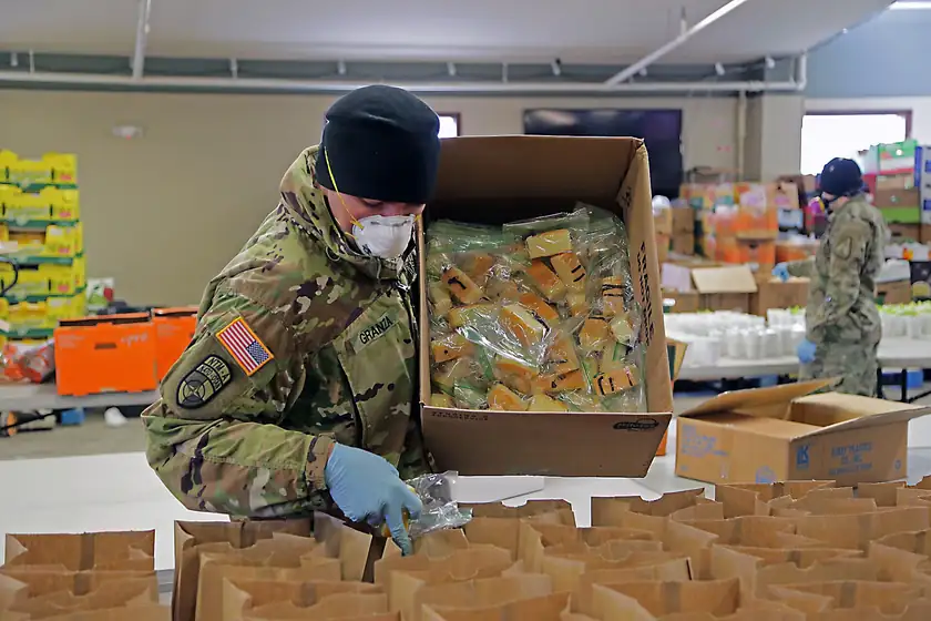 A person in uniform filling paper meal bags from a box of packaged food