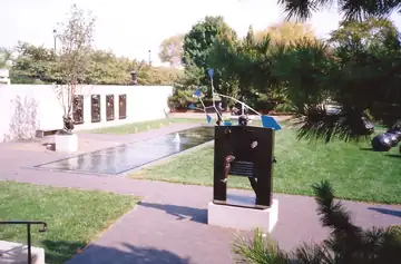A metal sculpture beside a reflecting pool in a walled garden