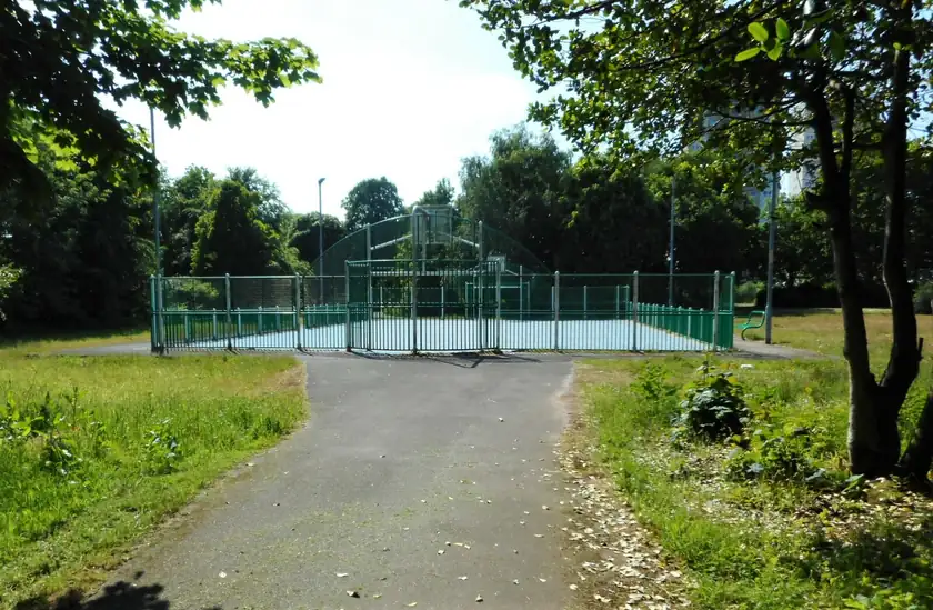 An empty outdoor basketball court in a leafy park