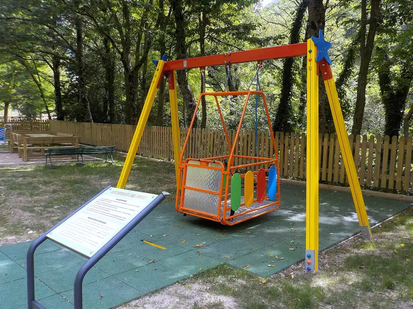 A bright orange wheelchair-accessible swing with a high back and a safety bar in a park